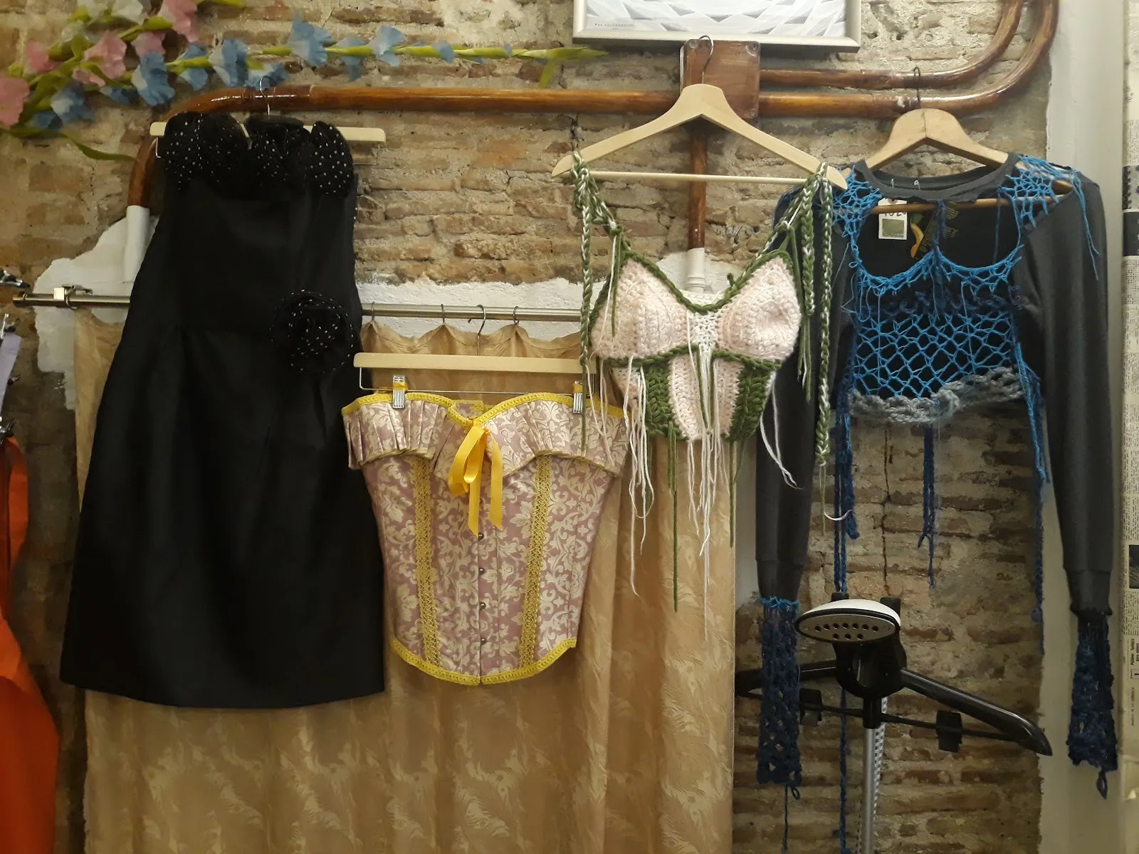 A black dress, a corset top and crochet tops hanging on a brick wall